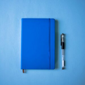 A blue notebook and a pen on a blue surface
