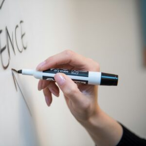 A hand writing on a whiteboard with a black dry-wipe marker