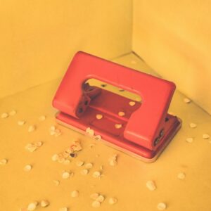 A red two-hole punch with paper punchings