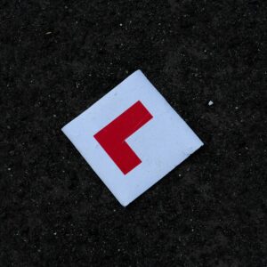 White square learner driver sign with a red L on dark tarmac