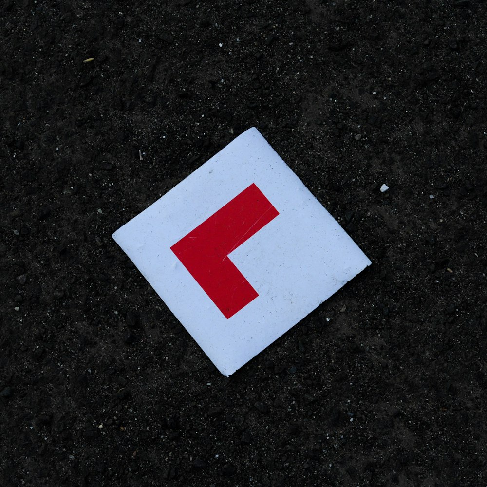 White square learner driver sign with a red L on dark tarmac