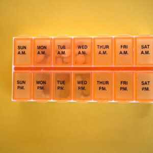 Orange weekly pill organiser with daily compartments on a yellow background