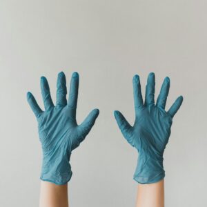 Two hands wearing blue nitrile gloves against a light grey background