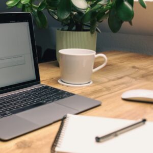 A laptop, notebook, phone and mug on a desk