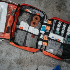 An open red first aid bag filled with medical supplies on a grey surface
