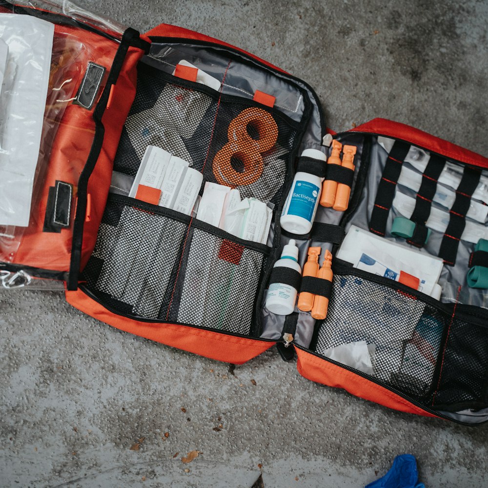 An open red first aid bag filled with medical supplies on a grey surface