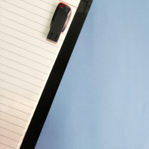 Black USB flash drive resting on a lined notebook against a blue background