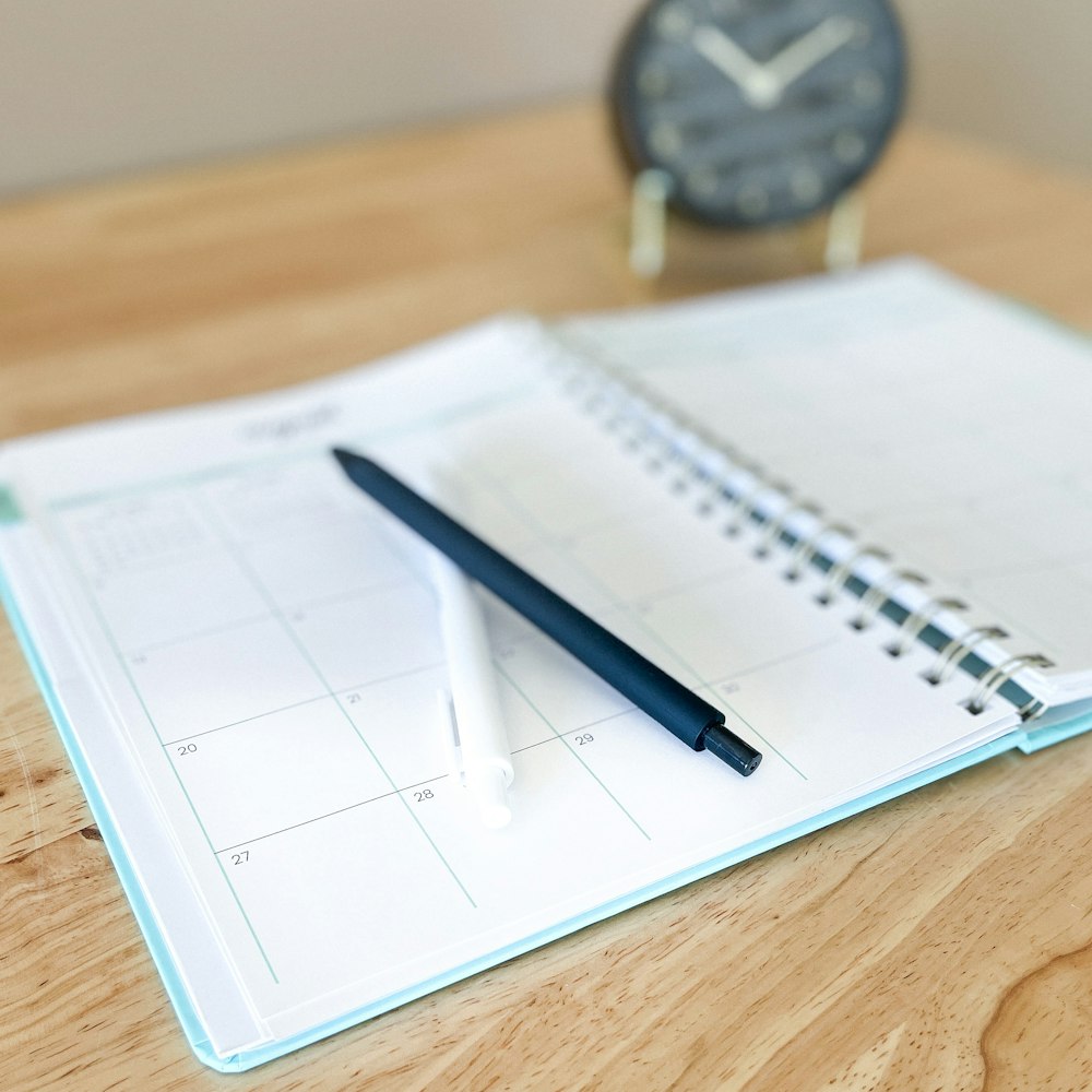 An open planner with a pen on a wooden desk
