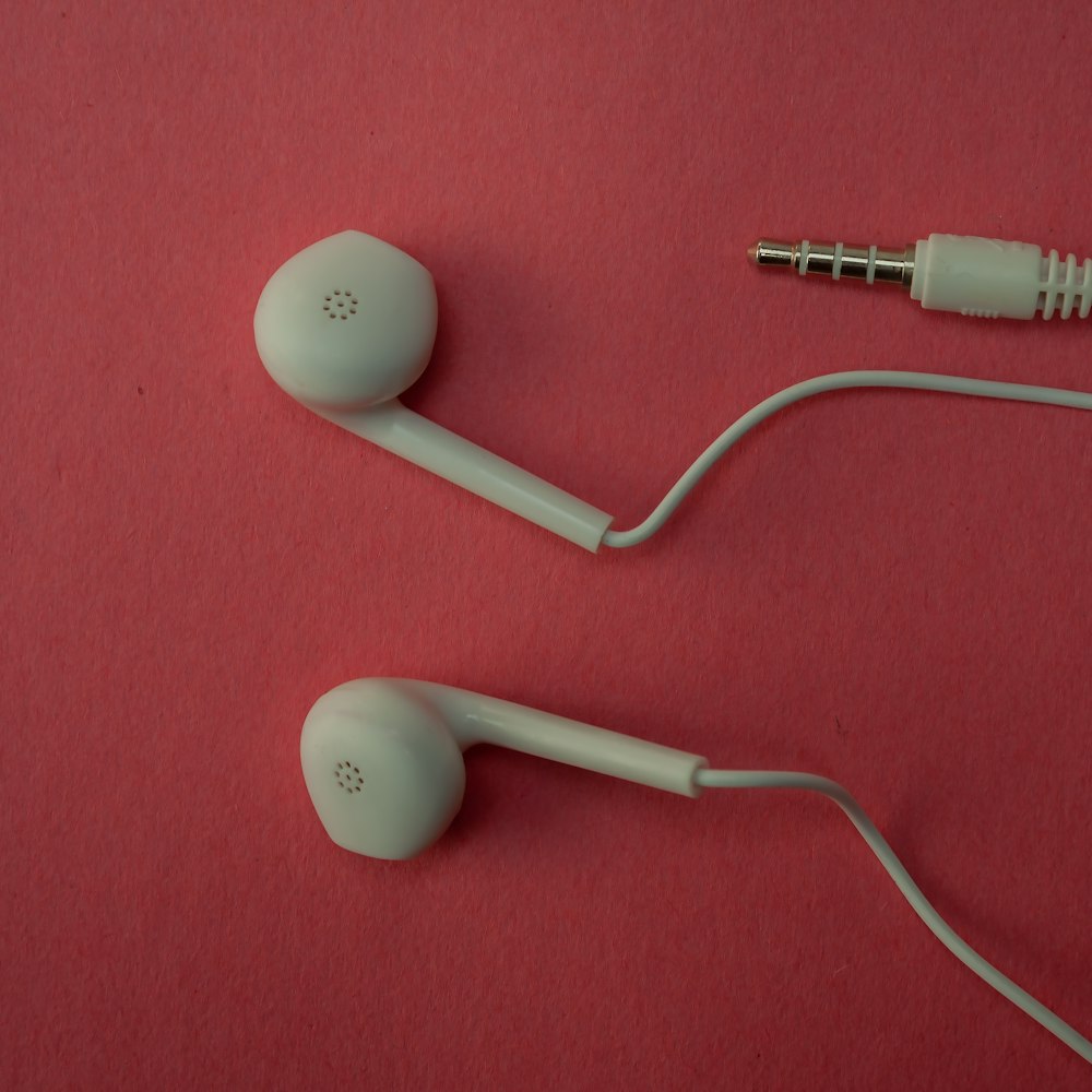White wired earphones and their cable on a pink surface
